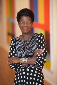 thelma smiling in black and white print dress in front of multicolor painting