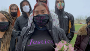 masked group holding flowers wearing 'justice' shirts