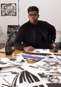 mark sitting at table covered in art on paper