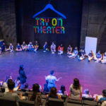 students seated in large circle on theater floor