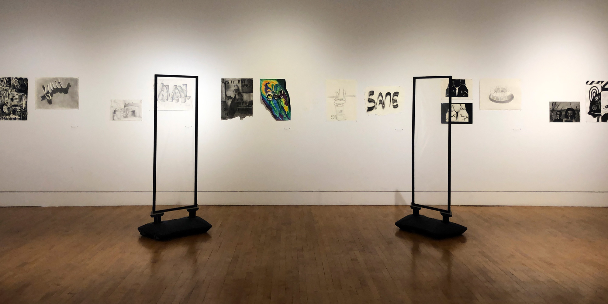 white gallery walls with small drawings and two large black standing frames on floor in foreground