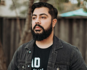 jamil with dark hair and beard looks off to left, wearing dark jacket