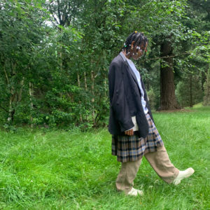 sidony in long jacket and pants walking on grass by trees