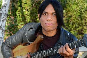 stanley jordan holds guitar and wears black leather jacket