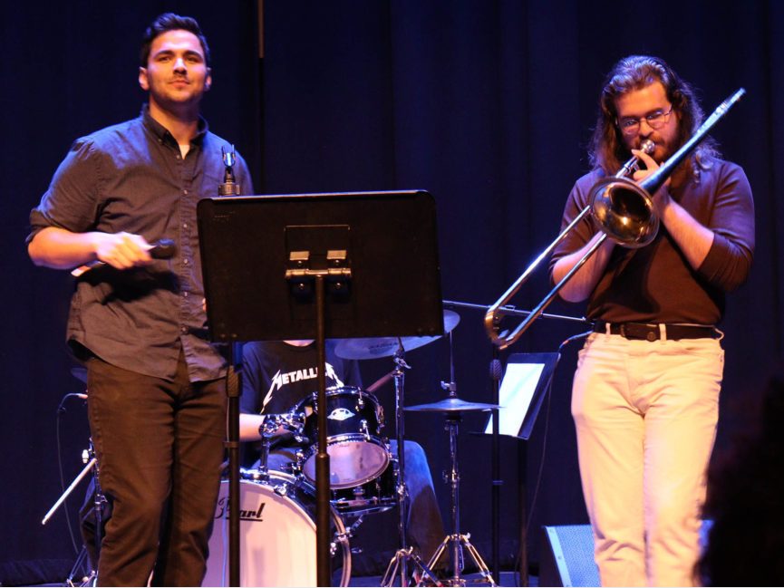 Someone sings as another performer plays trombone