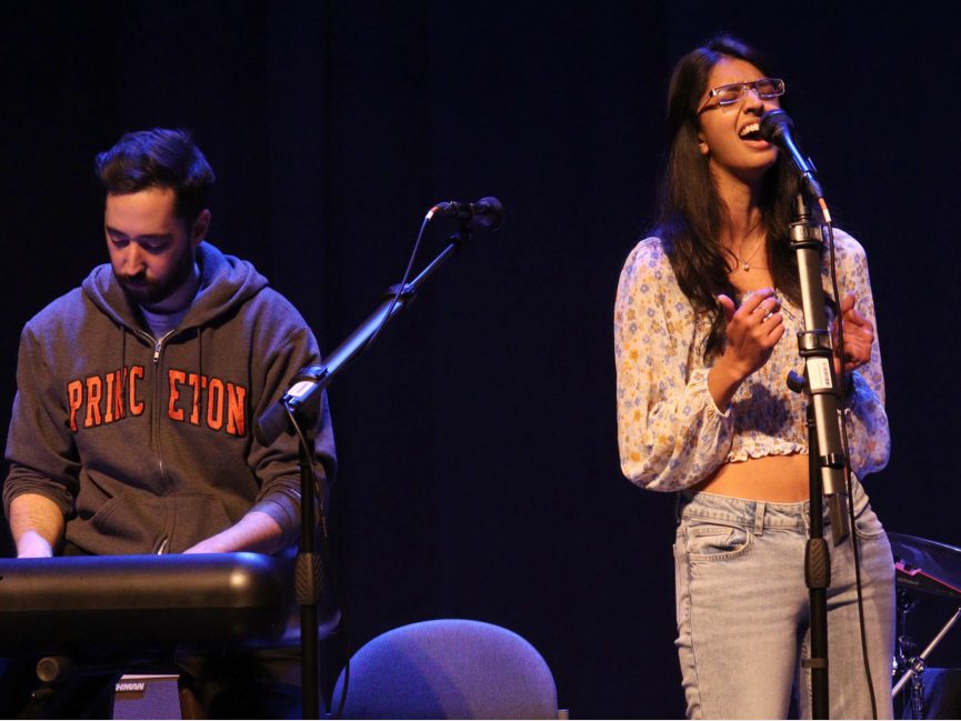 A performer plays on the keyboard as some sings passionately into a mic