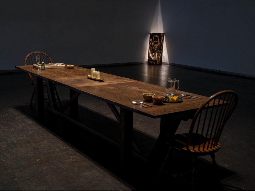 long wooden table sits in center of dark gallery
