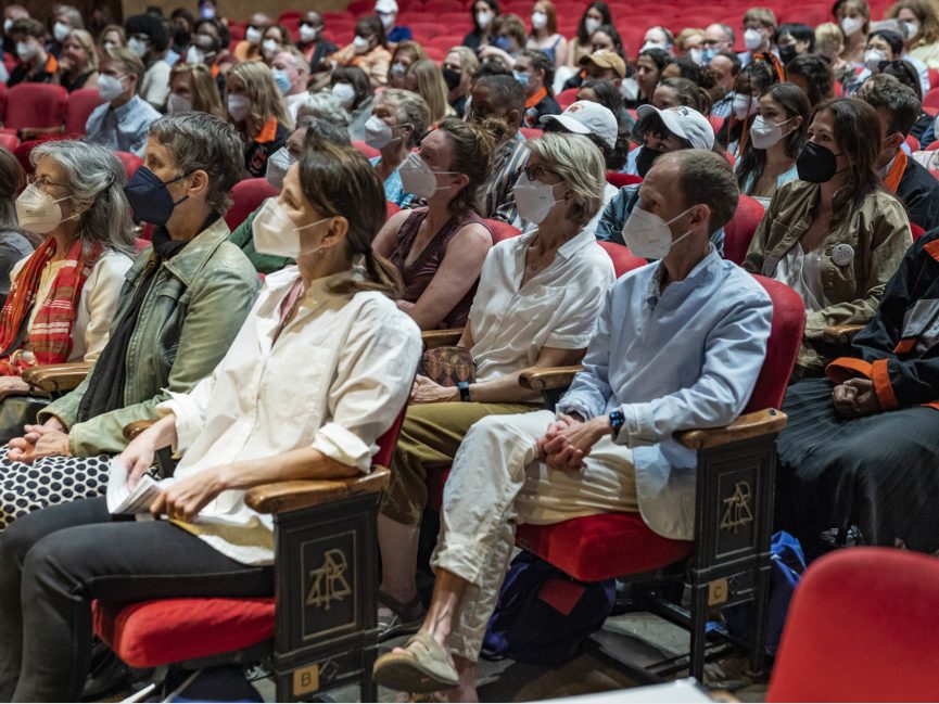 A crowd of people sit in chairs inside an auditorium