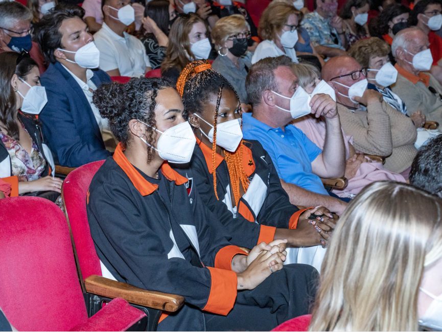 A crowd of people sit in chairs inside an auditorium