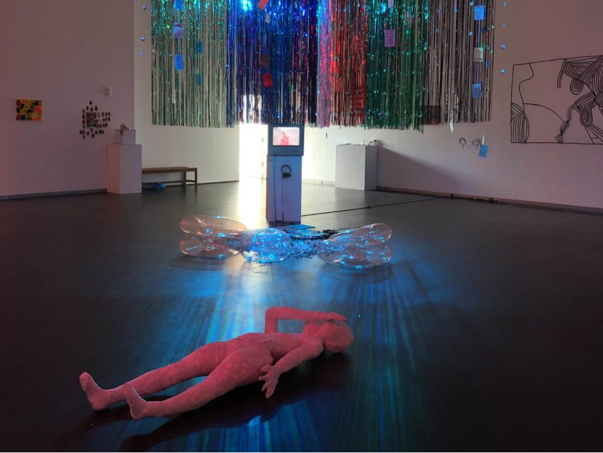 A sculpted figures lies on the ground as metallic streamers hang from the ceiling