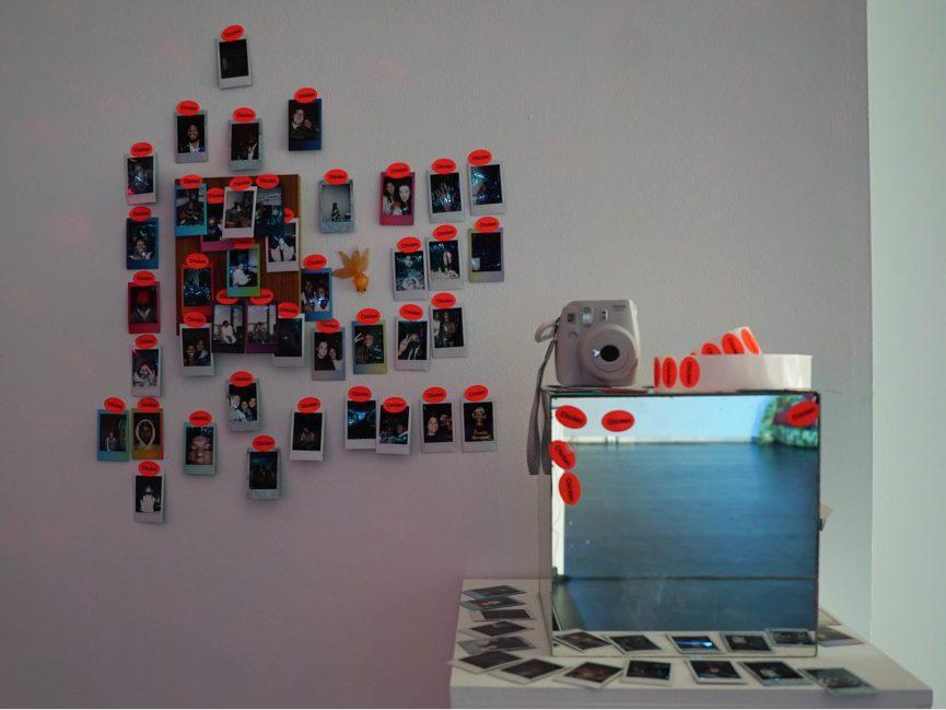Polaroids hang on the wall as a camera sits on a box