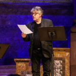 paul muldoon stands on richardson auditorium stage reading from a paper