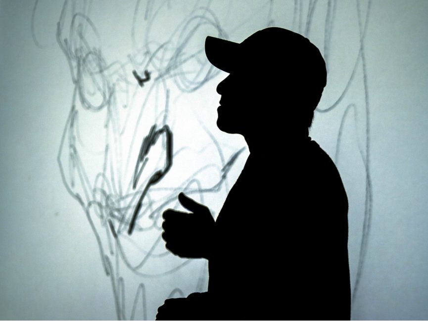A man is silhouetted by a projection of a drawing of the Joker