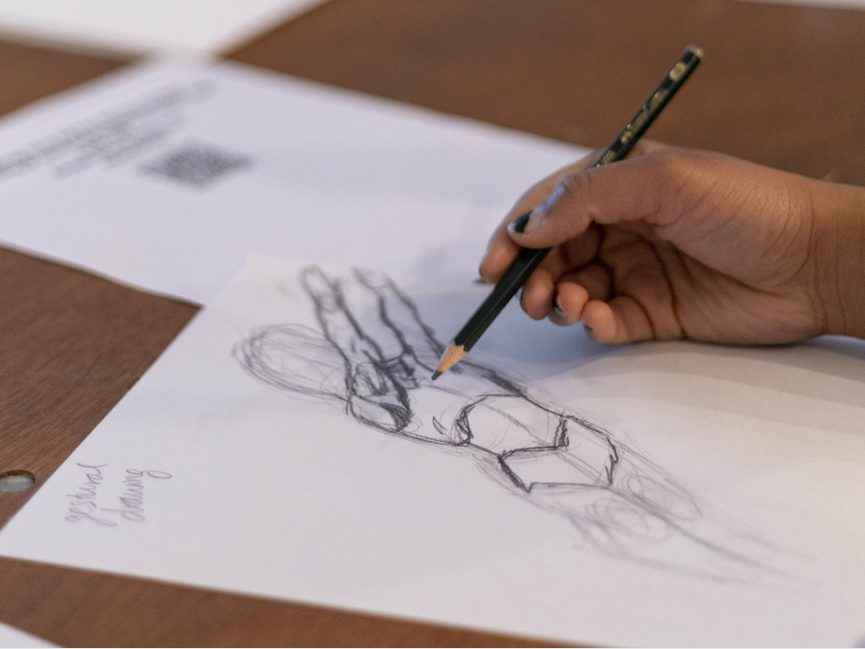 A hand holding a pencil draws a comic book figure