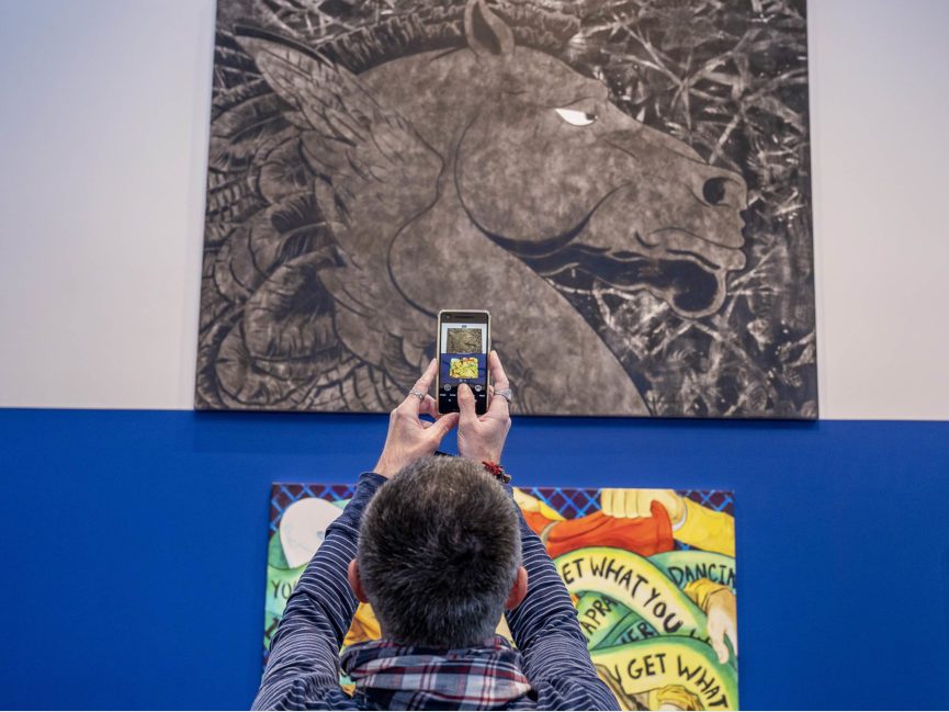 A person take a picture of artwork on a wall in a gallery