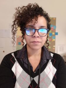 francine j. harris wears round glasses, a black argyle sweater, and has dark curly hair swept up on side of her face