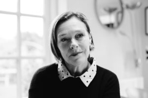 Alison Millar smiles slightly while looking off to her left. She wears her hair in a short bob and wears a black sweater with white polka dot collar shirt peeking out.