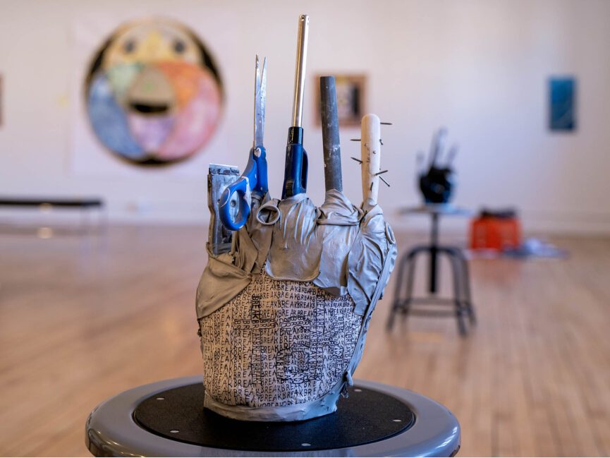 A sculpture that appears to be a hand with various tools as fingers sits on a chair