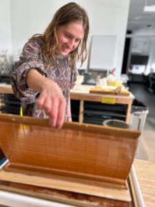 student lifts up a fresh paper piece with her two fingers to examine it in a workshop on papermaking
