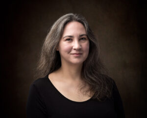 elizabeth boyle smiles with long dark wavy hair and wears a black blouse