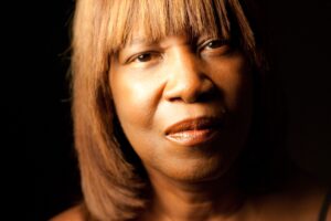 closeup portrait of Patricia Smith, with golden skin and hair with bangs framing her eyes.