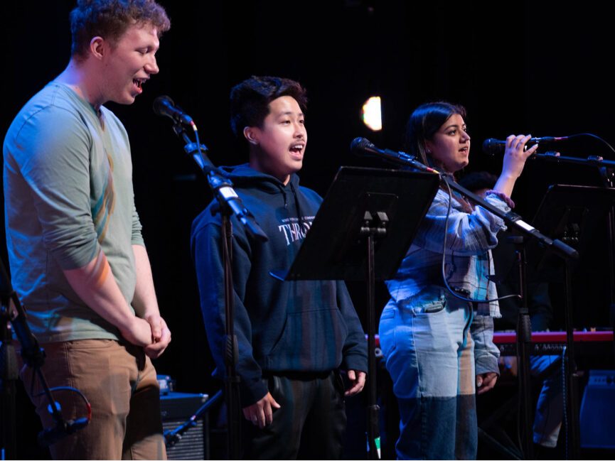 Three people perform and sing on stage