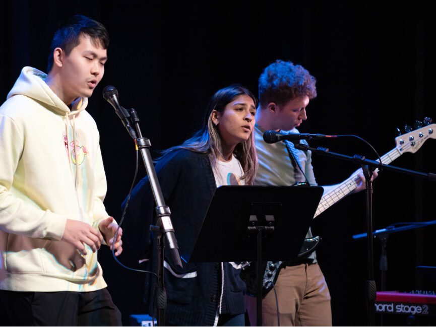 Three performers sing and play music on stage.