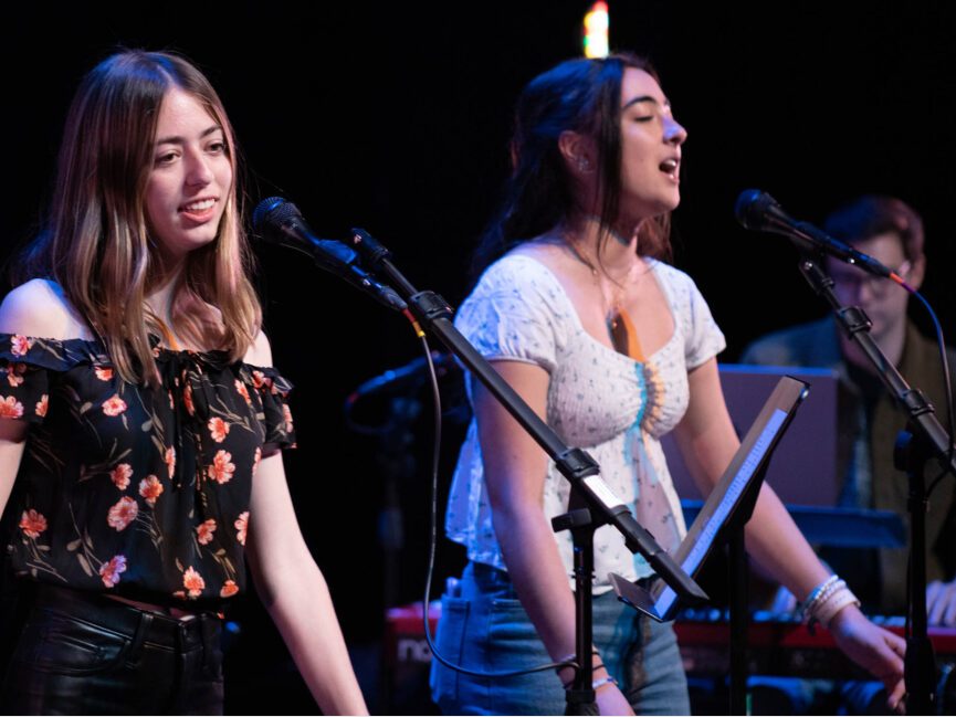 Two people sing into microphones on stage