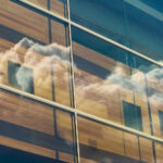Reflection of white clouds in a bright blue sky, seen through glass windows in the side of the Effron Music Building.