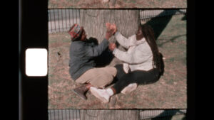 two people sit by a tree playing with their hands like a game of hand-clap