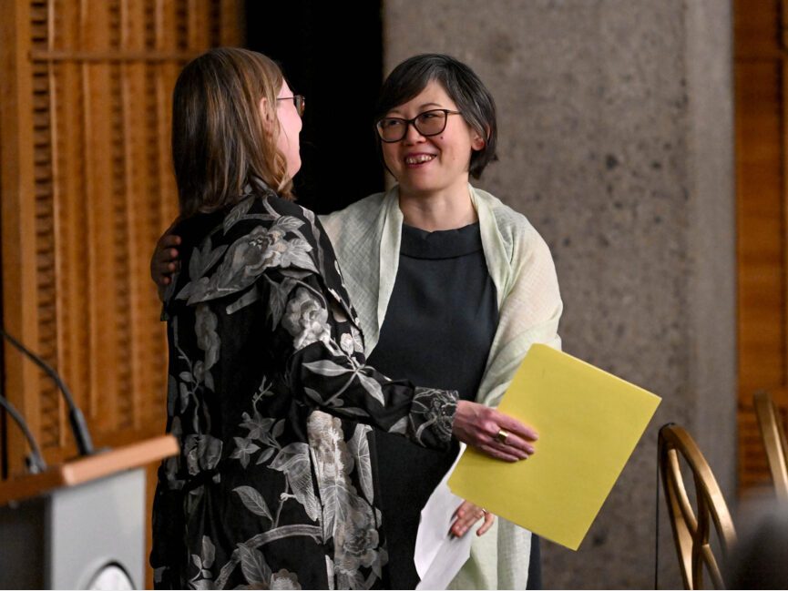 Two people prepare to hug in front of a podium at a formal gathering