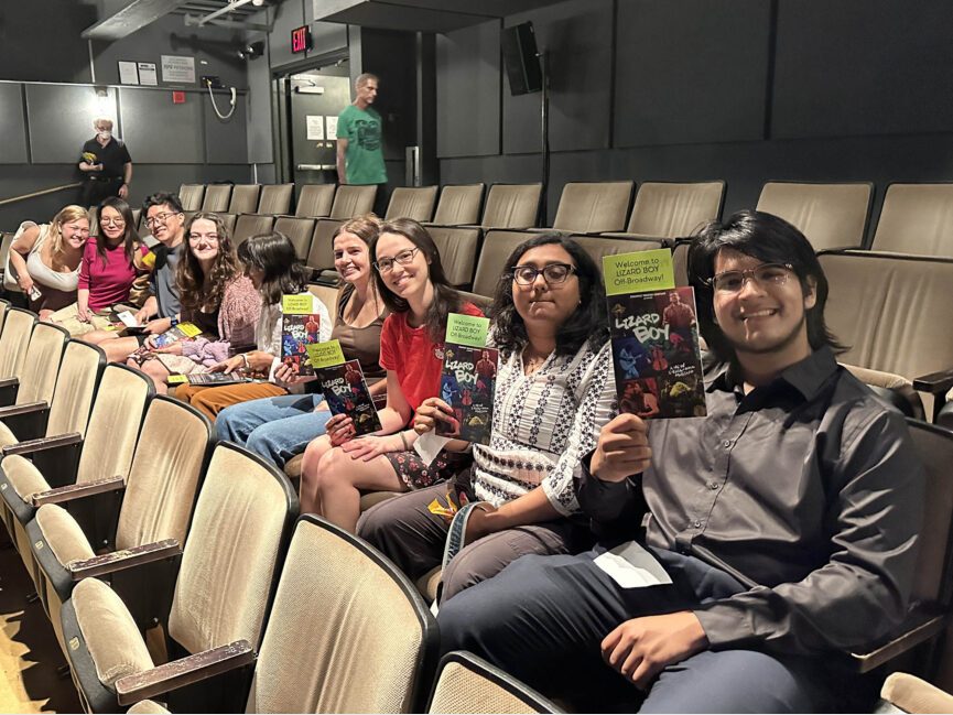 A row of students sit in theater seats holding programs.
