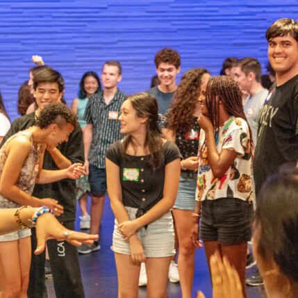 A large group of students mingle, talk and laugh in the Drapkin Studio during the community portion of Try on Theater Days.