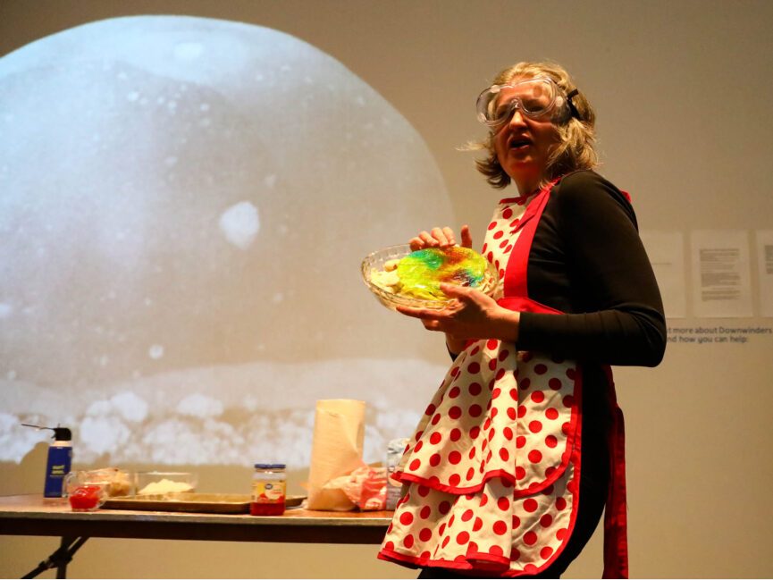 A performer in a colorful apron holds what appears to be a distorted multicolored pie