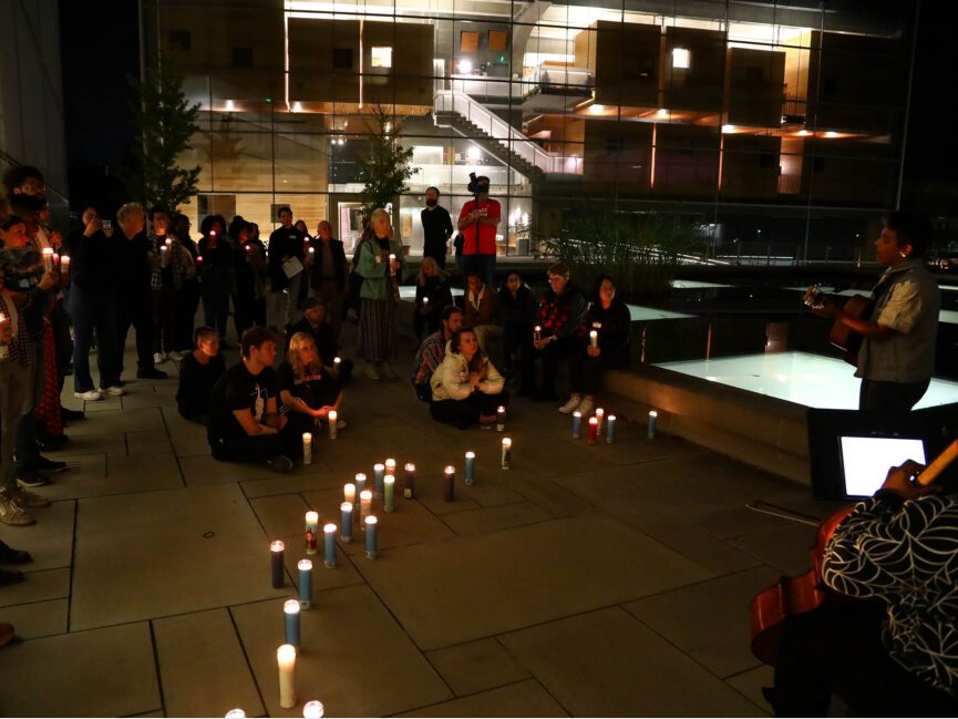 People sit and listen to musicians by candlelight at the Lewis Arts complex plaza.
