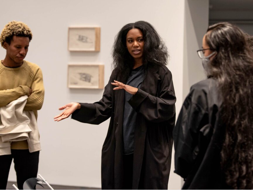 Artist sidony o’neal talks with exhibition visitors in a gallery with artwork on the walls