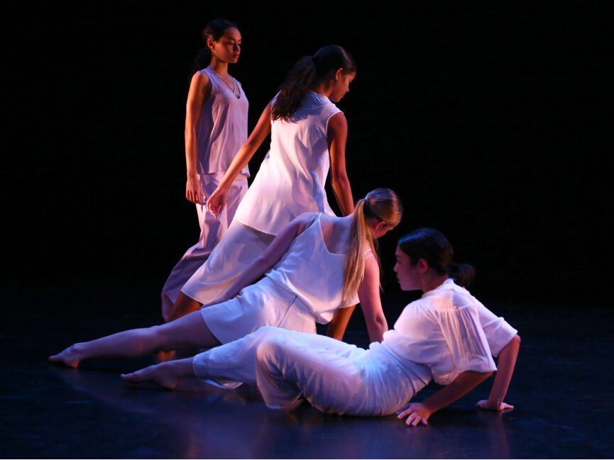 Four dancers in various positions from standing to lying on the floor.