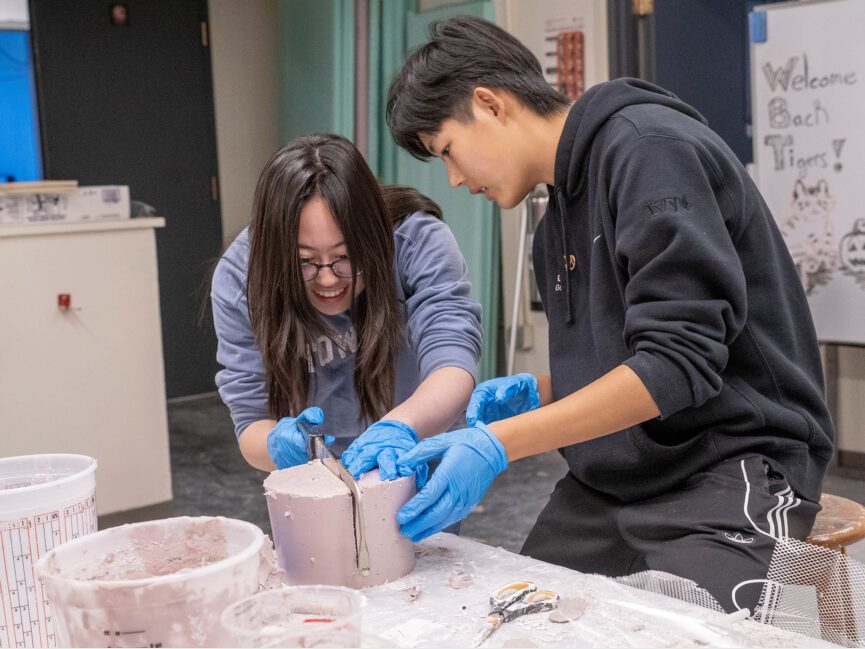 Two students cut open a mold with a saw trying to reveal what's underneath.