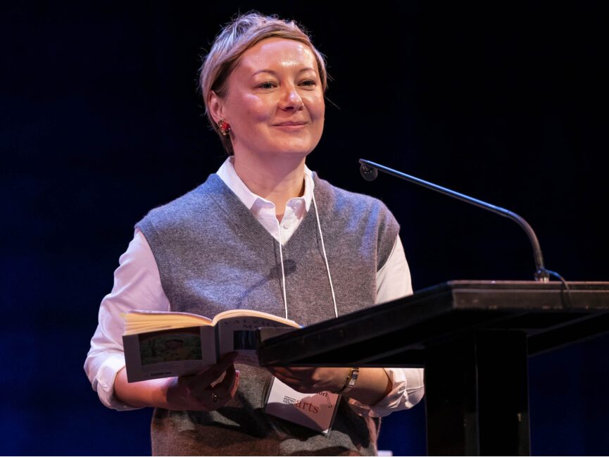 A poet stands at a podium with a book in hand