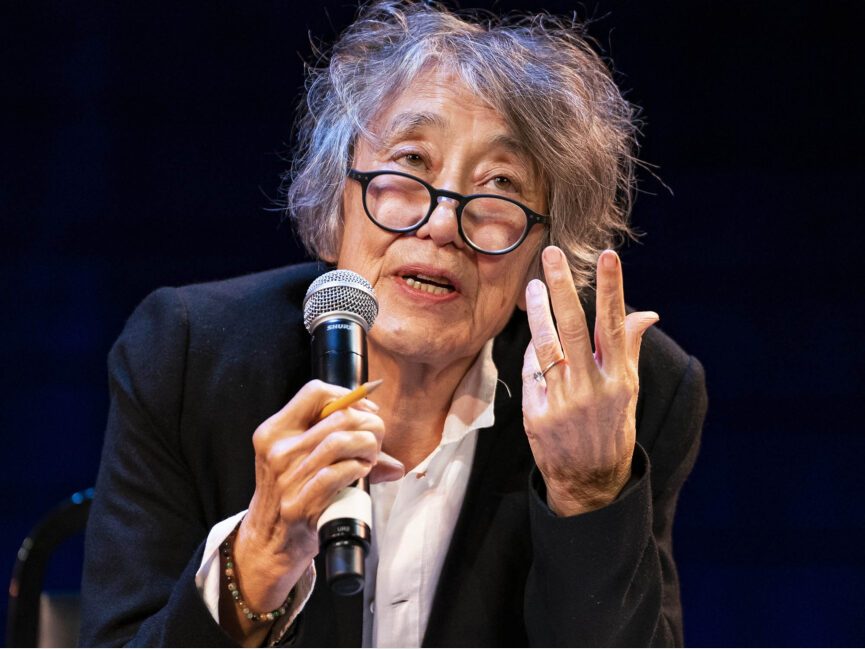 A poet holds a microphone in one hand and gestures with another to make a point.
