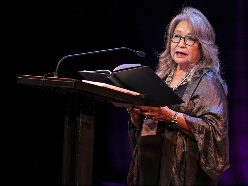 A poet stands at a podium with a book in hand