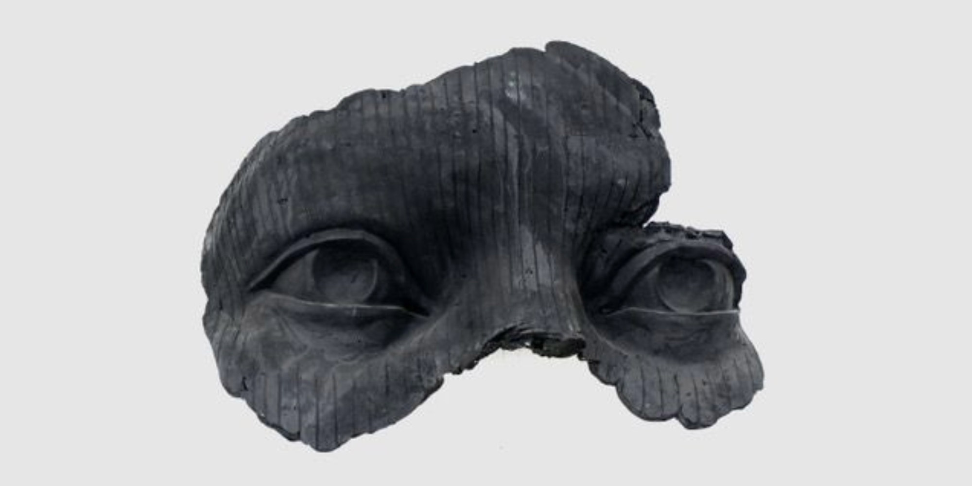 A black sculptural fragment of a face with both eyes and part of the nose, as in a mask.