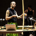 A performer plays an assortment of musical instruments in the center of a circular desk