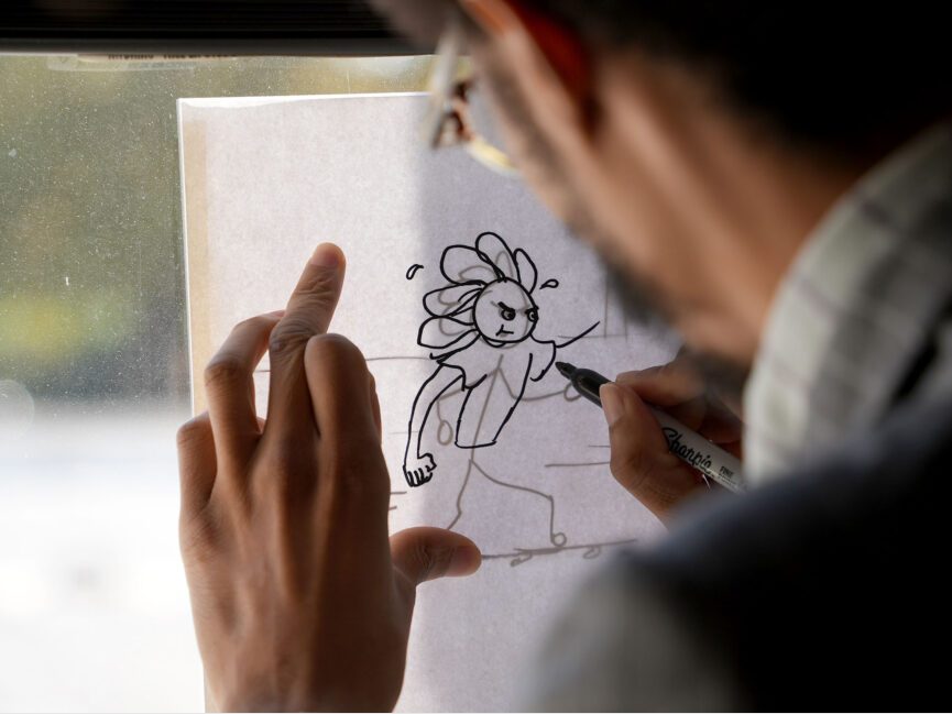 E.S. Glenn traces a cartoon figure on a piece of paper that has been back lit by an outside wondow