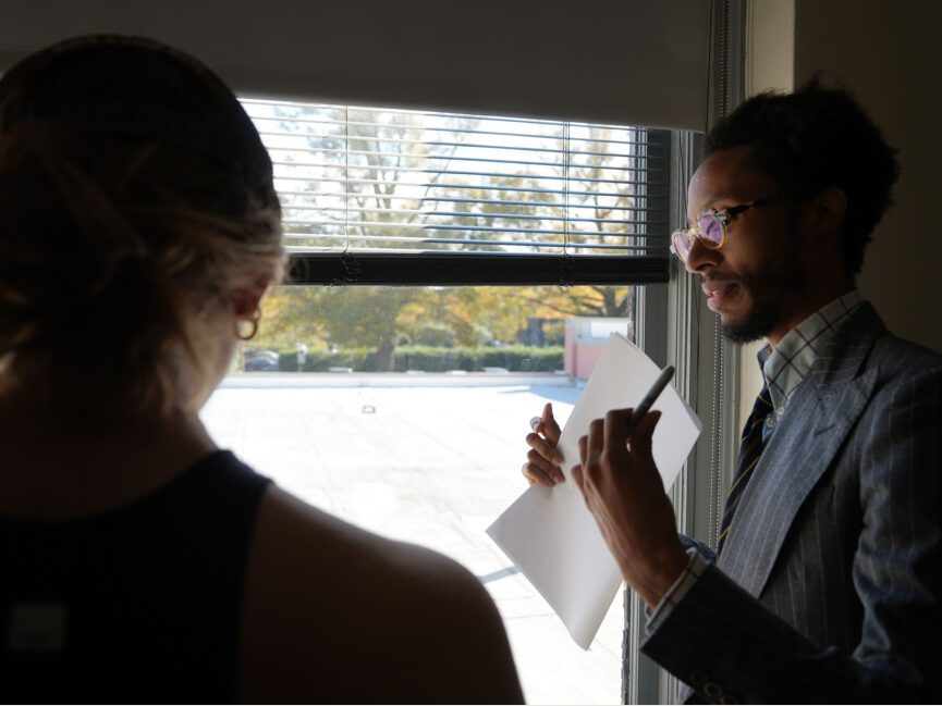 E.S. Glenn stands by a window and works with a student on their illustration