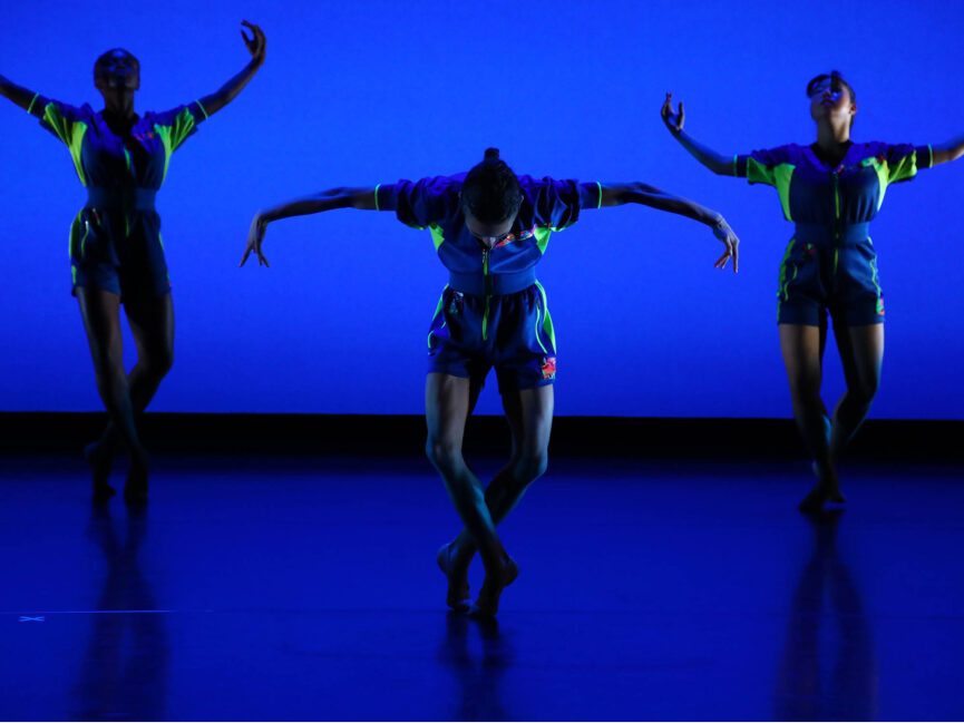 A center dancer with legs crossed and arms and head pointed downwards is flanked by 2 dancers doing the opposite motion