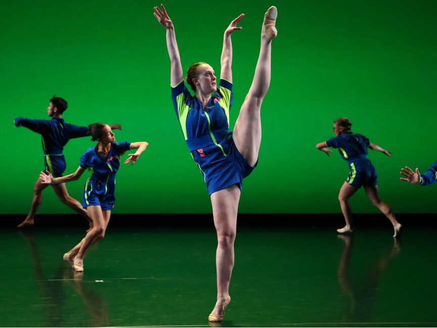 A dancer center stage kicks a leg high in the air