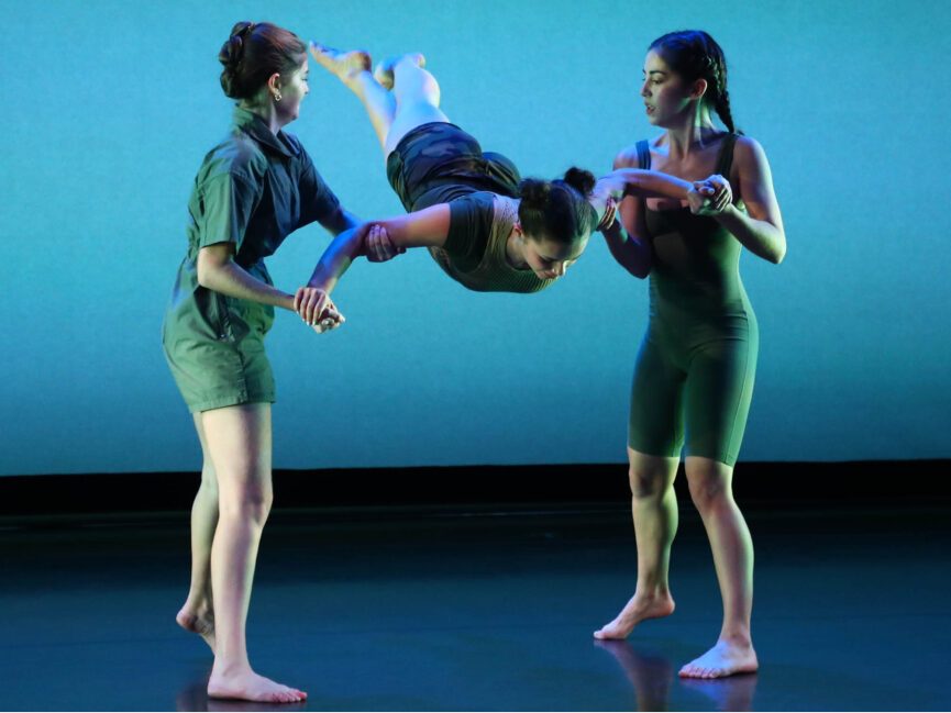 Two dancers hold a third dancer in the middle
