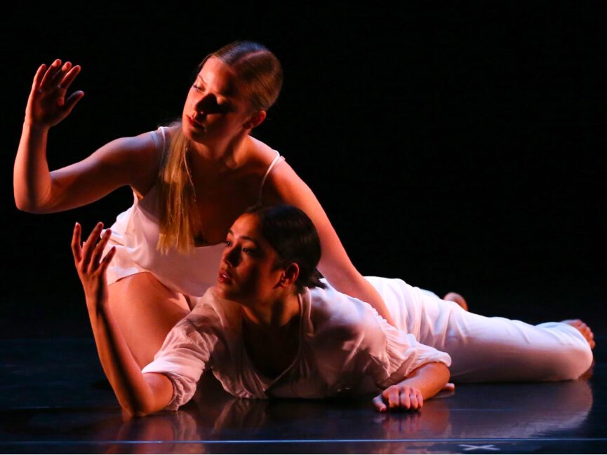 Two dancers lie on the floor and look out to their outstretched hands.