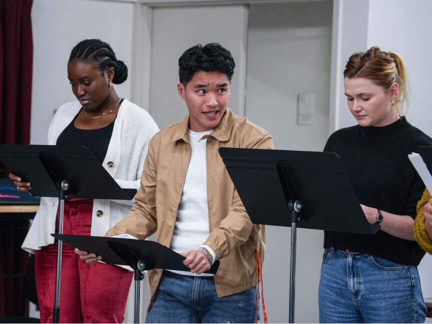 Three people read scripts on music stands